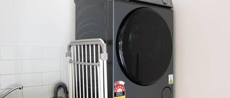 Lavadora compacta y moderna con puerta frontal, ubicada al lado de un lavamanos de acero inoxidable en una cocina.