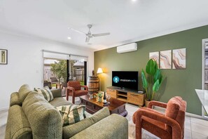 A modern living room with a television, sofas, a coffee table, and a ceiling fan. - Stylish 4BR Sleeps Up To 8 Near Theme Parks (Coomera)