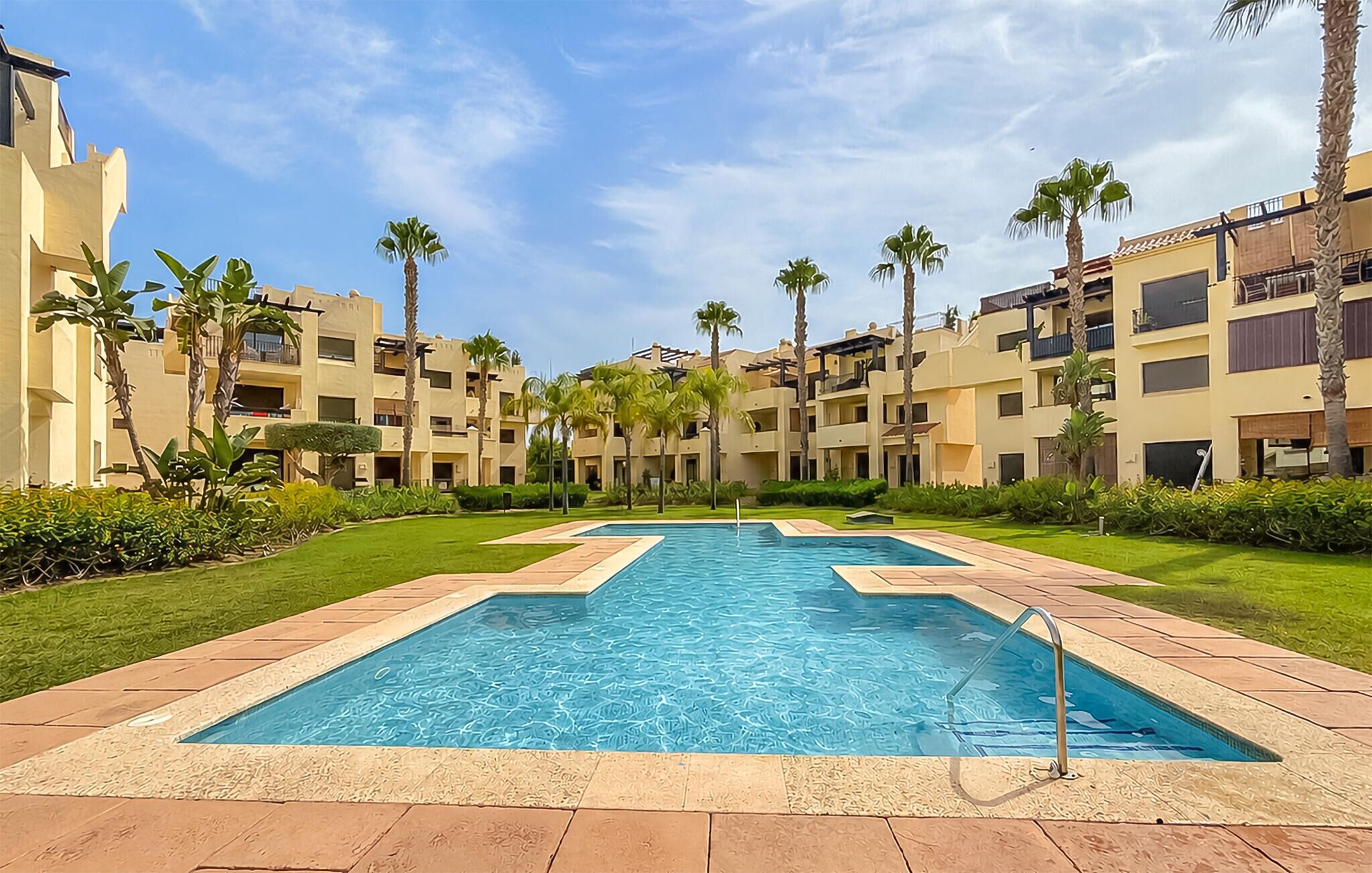 A swimming pool surrounded by palm trees and a multi-story building with balconies.
