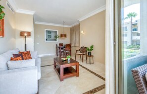 A modern living room with a sofa, coffee table, dining area, and a view of a building through a glass door. - Beautiful apartment in San Javier with WiFi (San Javier)