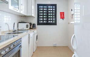 A compact kitchen with white appliances, a coffee maker, a microwave, and a window with a fire blanket sign. - Beautiful apartment in San Javier with WiFi (San Javier)