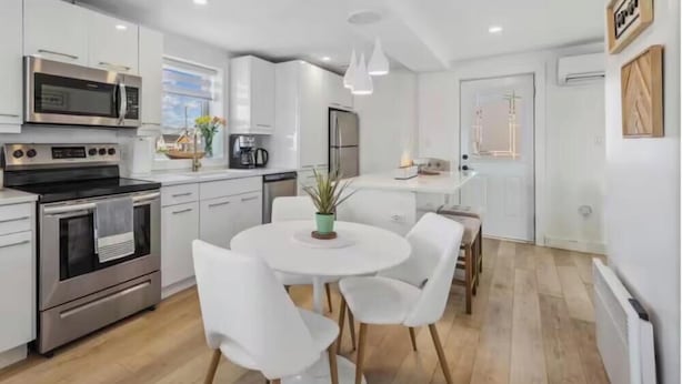 A modern kitchen with white cabinetry, stainless steel appliances, a round dining table with white chairs, and a potted plant.