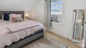 A bedroom with a bed, bedside lamps, a window with curtains, and a door.
