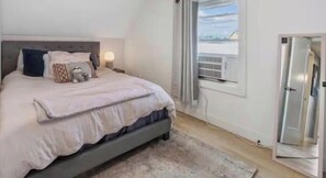 A bedroom with a bed, bedside lamps, a window with curtains, and a door.