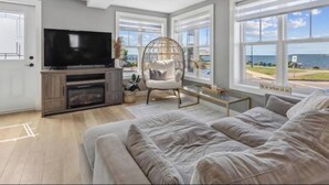 A living room with a large flat-screen TV, a fireplace, a comfortable sofa, a hanging chair, and a view of the sea through large windows.