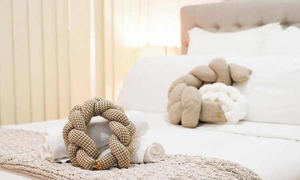 A neatly made bed with a white comforter and pillows, a knitted throw blanket, and a decorative braided item on the bed. - KozyGuru | Parramatta | Prime City Centre Living (Parramatta)