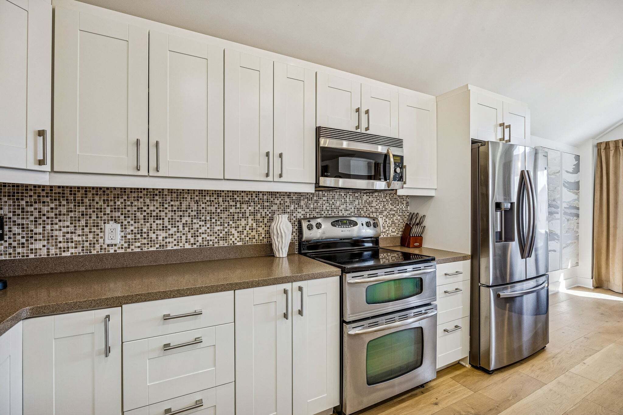 A modern kitchen with white cabinets, a stainless steel refrigerator, a microwave, and a stove.