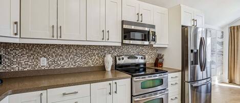 A modern kitchen with white cabinets, a stainless steel refrigerator, a microwave, and a stove.