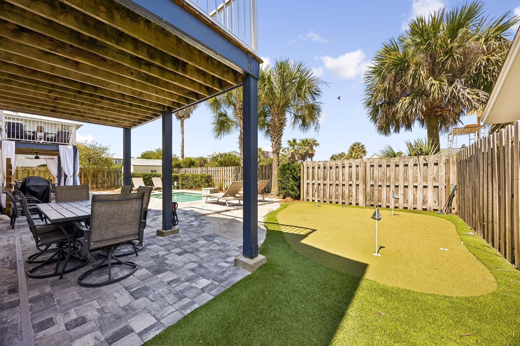 A covered patio with outdoor furniture, a pool, and a well-maintained lawn.