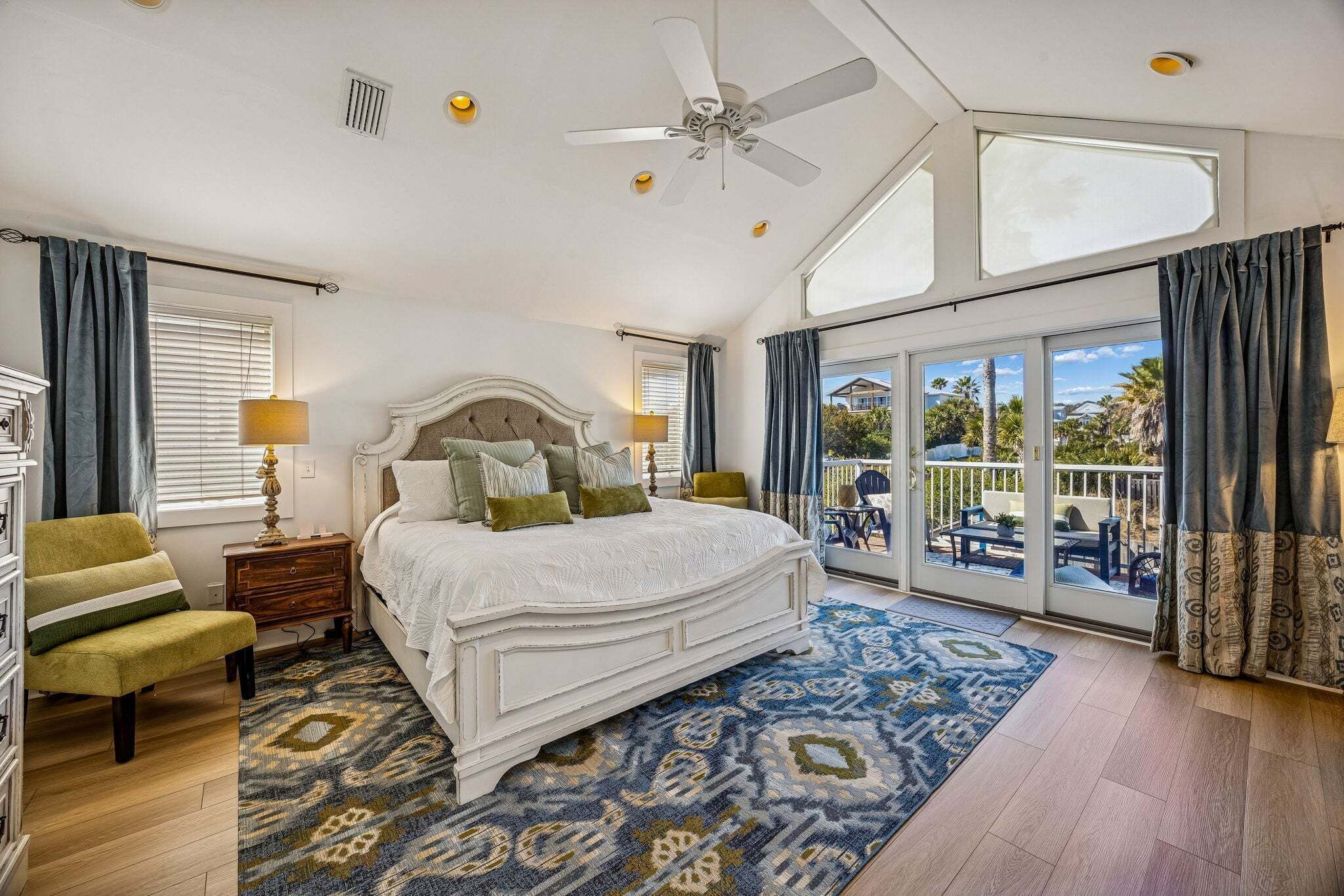 A bedroom with a large bed, a ceiling fan, and a view through a sliding glass door to an outdoor area.