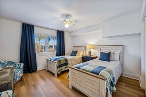 A hotel room with two beds, a ceiling fan, a window with curtains, a bedside table with a lamp, and a patterned rug. - Remodeled & modern coastal escape duplex with pool, close to beach (Fernandina Beach)