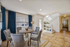 A dining area with a round table and four chairs, a staircase, and a bookshelf with decorative items. - Remodeled & modern coastal escape duplex with pool, close to beach (Fernandina Beach)