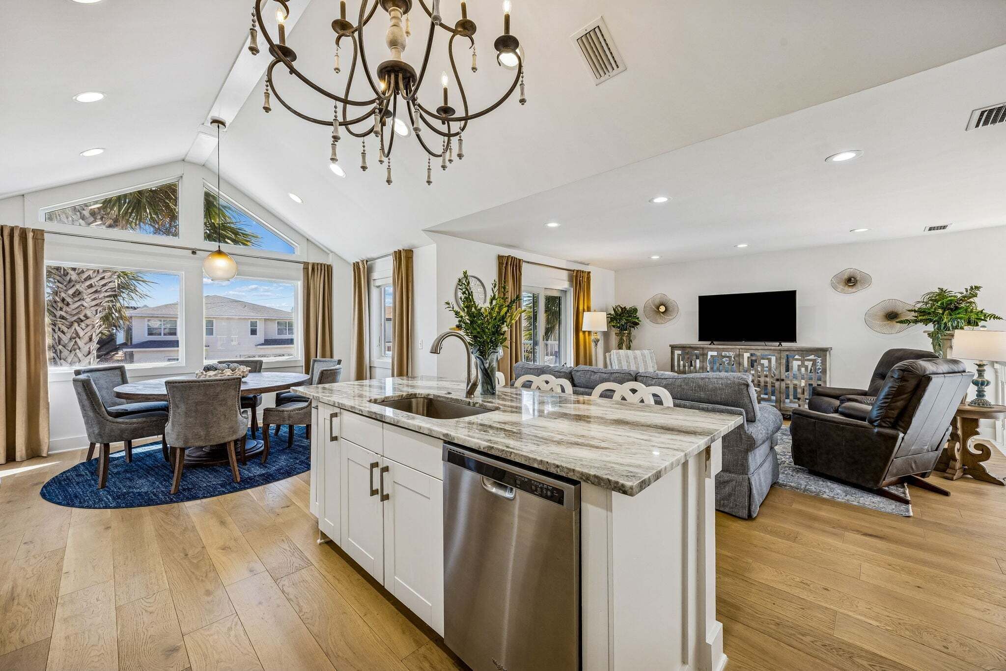 A modern kitchen with a central island, dining area with chairs, and a living room with a sofa and TV.
