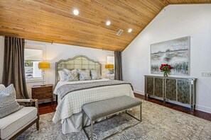 A bedroom with a large bed, bedside lamps, a bench, a dresser, and a painting on the wall. - Spectacular renovated duplex with pool near beach (Fernandina Beach)