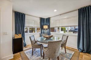 A dining area with a round glass table, four upholstered chairs, a floor lamp, and a view of the outside through large windows with blinds. - Spectacular renovated duplex with pool near beach (Fernandina Beach)