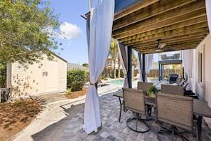 Ein überdachter Patio-Bereich mit Pool, Gartenmöbeln und einer Pergola.