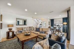A spacious living room with a large L-shaped sofa, a coffee table, and a dining area with a table and chairs. - Spectacular renovated duplex with pool near beach (Fernandina Beach)