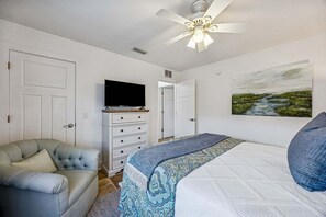 Ein Schlafzimmer mit einem Bett, einem Fernseher auf einer Kommode, einem Sessel und einem Bild an der Wand.