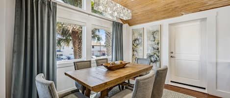 A dining area with a wooden table and four upholstered chairs, a window with curtains, and a door with artwork on the wall.