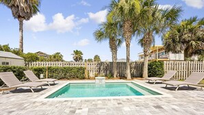 Una piscina rectangular con un deck de piedra, rodeada de sillas de descanso y palmeras.