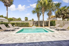 Ein rechteckiger Pool mit einer Steindeckplatte, umgeben von Liegestühlen und Palmen.