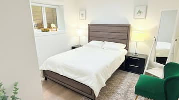 Une chambre à coucher avec un lit, des tables de chevet, un miroir, un fauteuil vert et une fenêtre donnant sur un beau paysage.