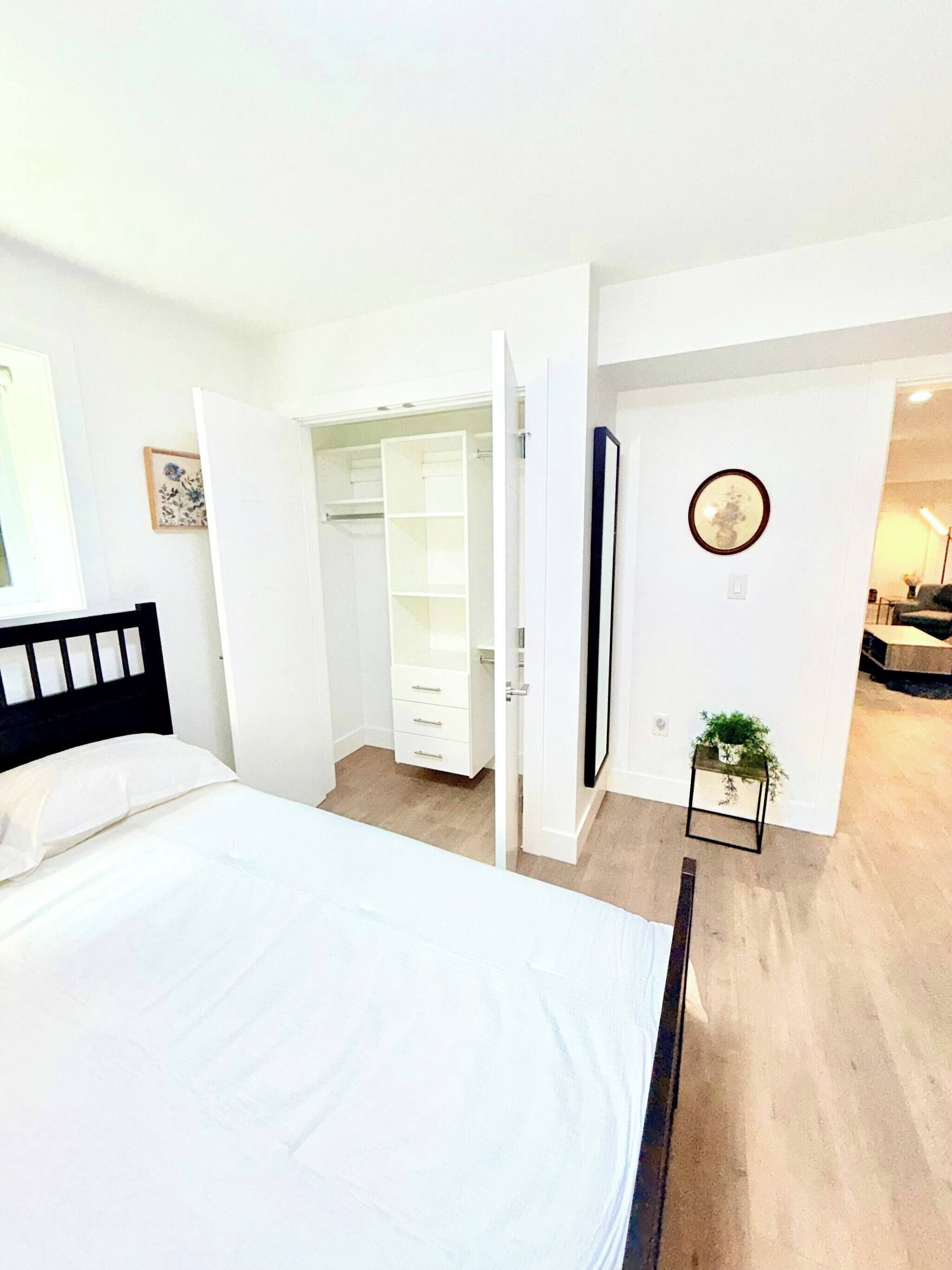 A bedroom with a bed, a walk-in closet, and a small plant on the wall.