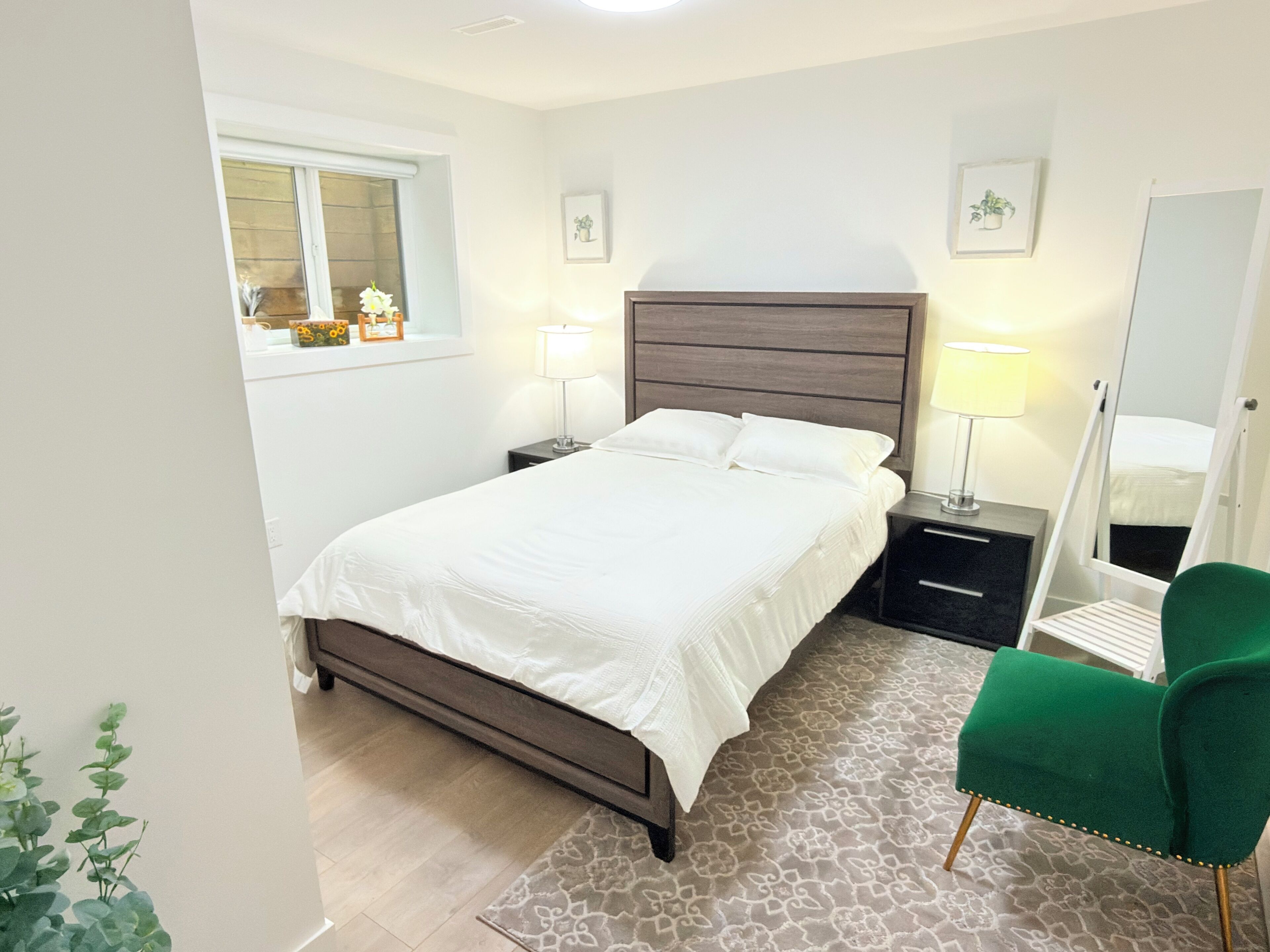 A bedroom with a bed, bedside tables, a mirror, a green chair, and a window.