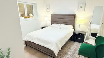A bedroom with a bed, bedside tables, a mirror, a green chair, and a window.