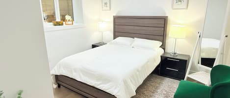 Een slaapkamer met een bed, nachtkastjes, een spiegel, een groene stoel en een raam.