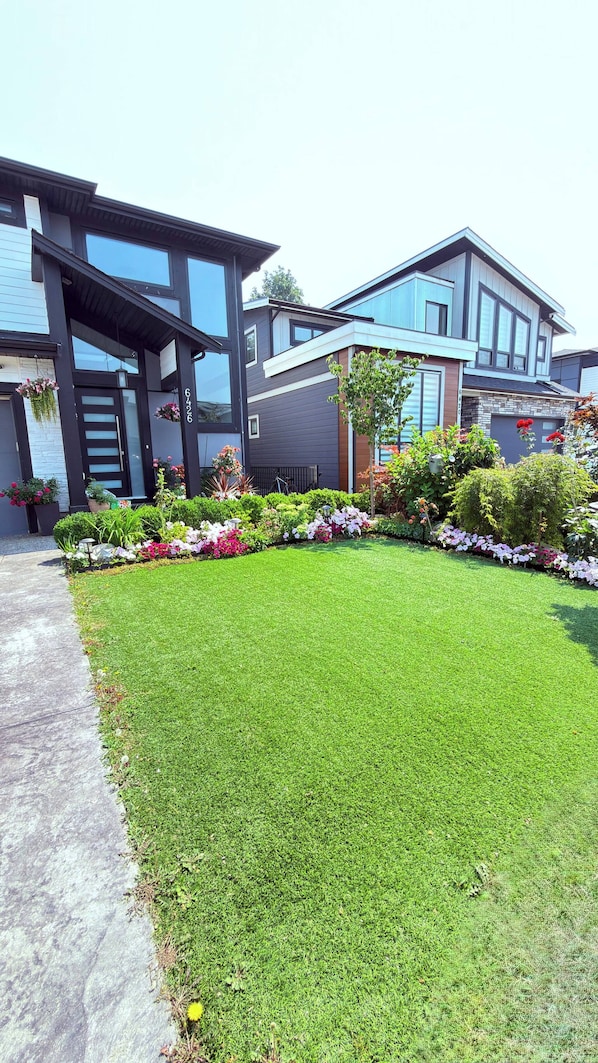 Una casa moderna de dos pisos con un césped cuidado y diversas plantas florecientes.