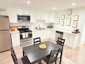 Una cocina moderna con armarios blancos, electrodomésticos de acero inoxidable y un comedor con una mesa y sillas oscuras.