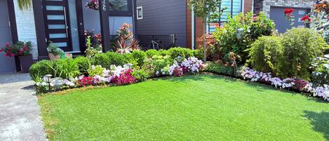 A modern two-story house with a well-maintained lawn and a variety of flowering plants.