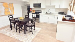 Una cocina moderna con armarios blancos, una mesa de comedor con sillas y un microondas sobre la estufa.