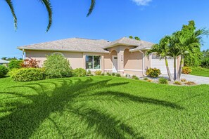 A single-story house with a front yard, a garage, and a driveway. - Sunset Villa 1035 Modern Waterfront Heated Pool Home w/ Fire Pit (Cape Coral)