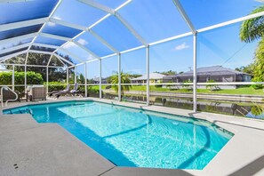 A pool with a covered area, clear blue water, and a view of the surrounding landscape. - Sunset Villa 1035 Modern Waterfront Heated Pool Home w/ Fire Pit (Cape Coral)