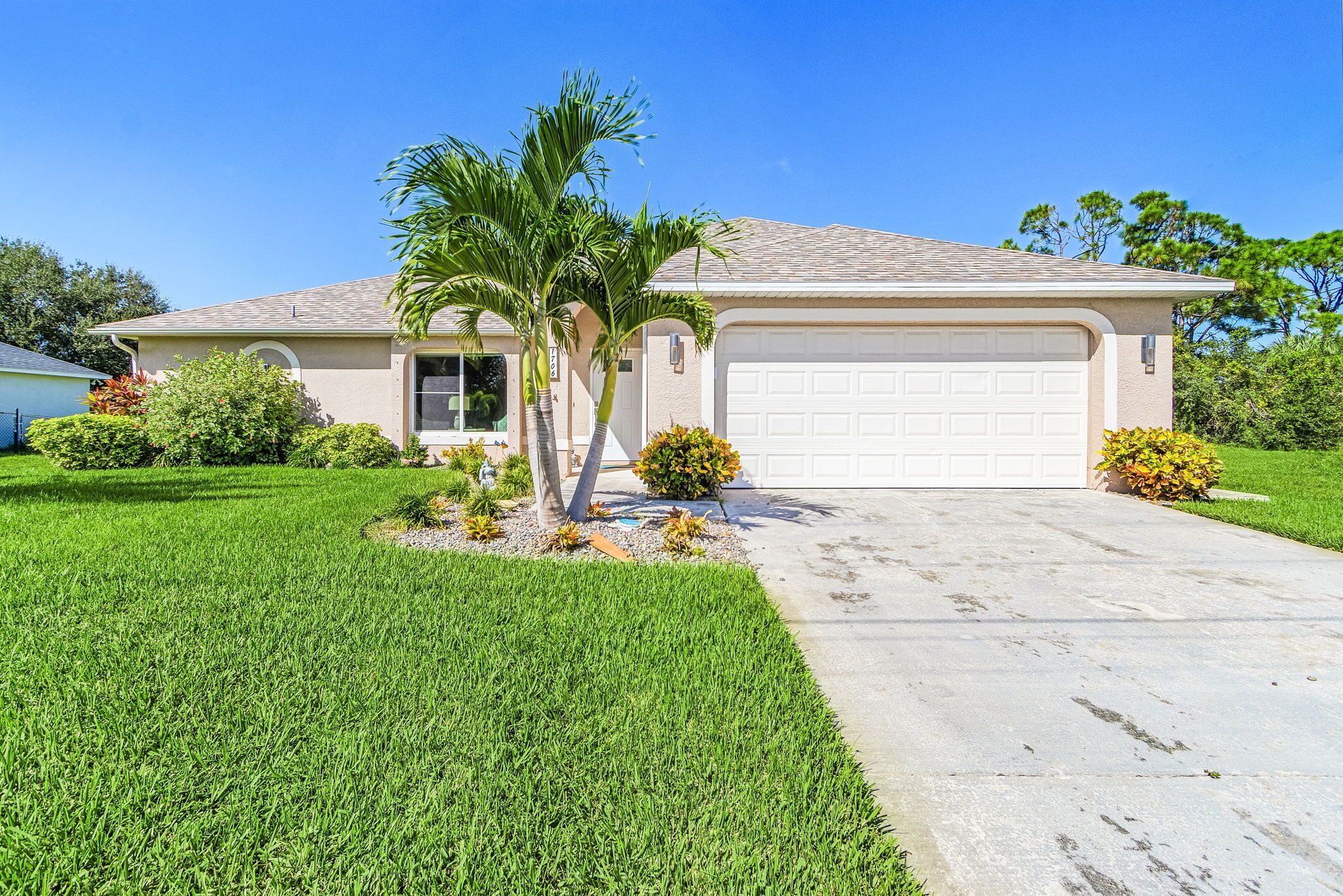 A single-story house with a garage, a well-maintained lawn, and a palm tree.