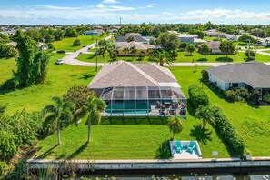 A residential area with houses, a swimming pool, and a large glass structure. - Sunset Villa 1035 Modern Waterfront Heated Pool Home w/ Fire Pit (Cape Coral)
