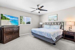 Een slaapkamer met een bed, een plafondventilator, een televisie, een dressoir, een nachtkastje en een raam.