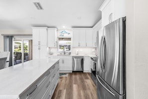 A modern kitchen with white cabinetry, stainless steel appliances, and a large island. - Sunset Villa 1035 Modern Waterfront Heated Pool Home w/ Fire Pit (Cape Coral)