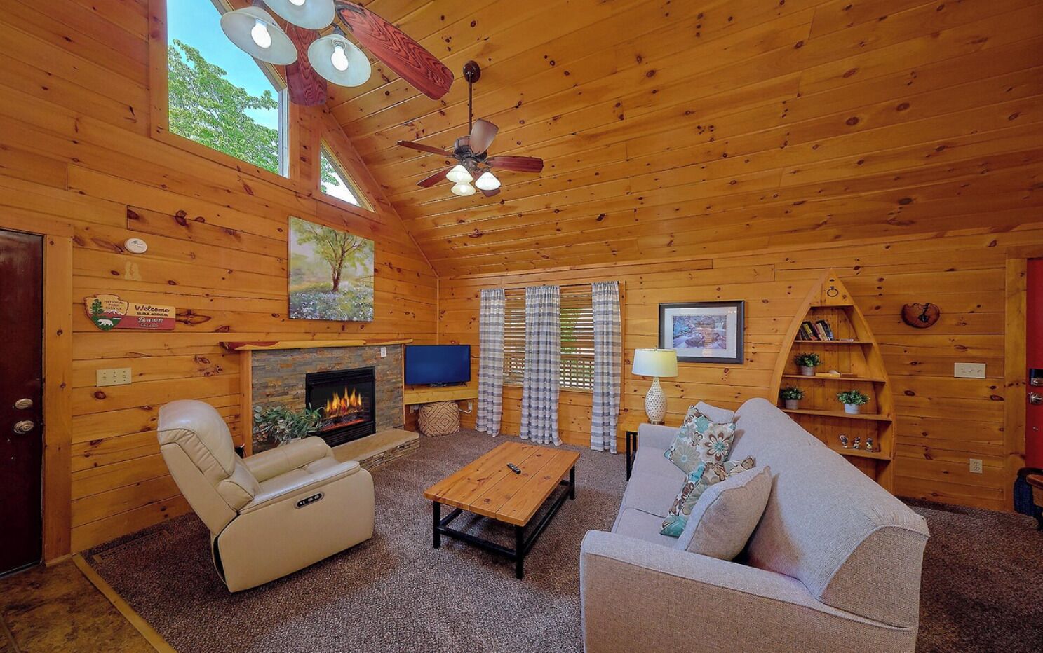 A cozy log cabin interior with a fireplace, leather sofa, wooden coffee table, and a ceiling fan.