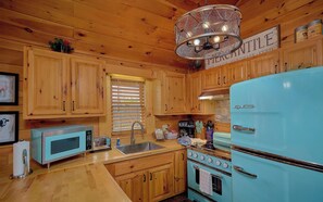 Eine Küche mit Holzausstattung, einem blauen Kühlschrank, einer Mikrowelle und einem Spülbecken.