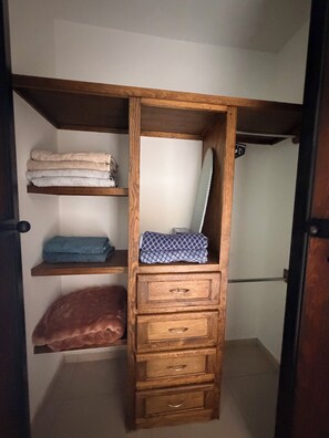 A wooden wardrobe with multiple shelves and drawers, containing folded towels and a mirror.