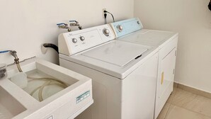 A white washing machine with a control panel, a sink with a faucet, and a wall-mounted electrical outlet. - Adorable 2-bedroom apartment in lovely Jalostotitlán perfect for relaxing (Jalostotitlán)