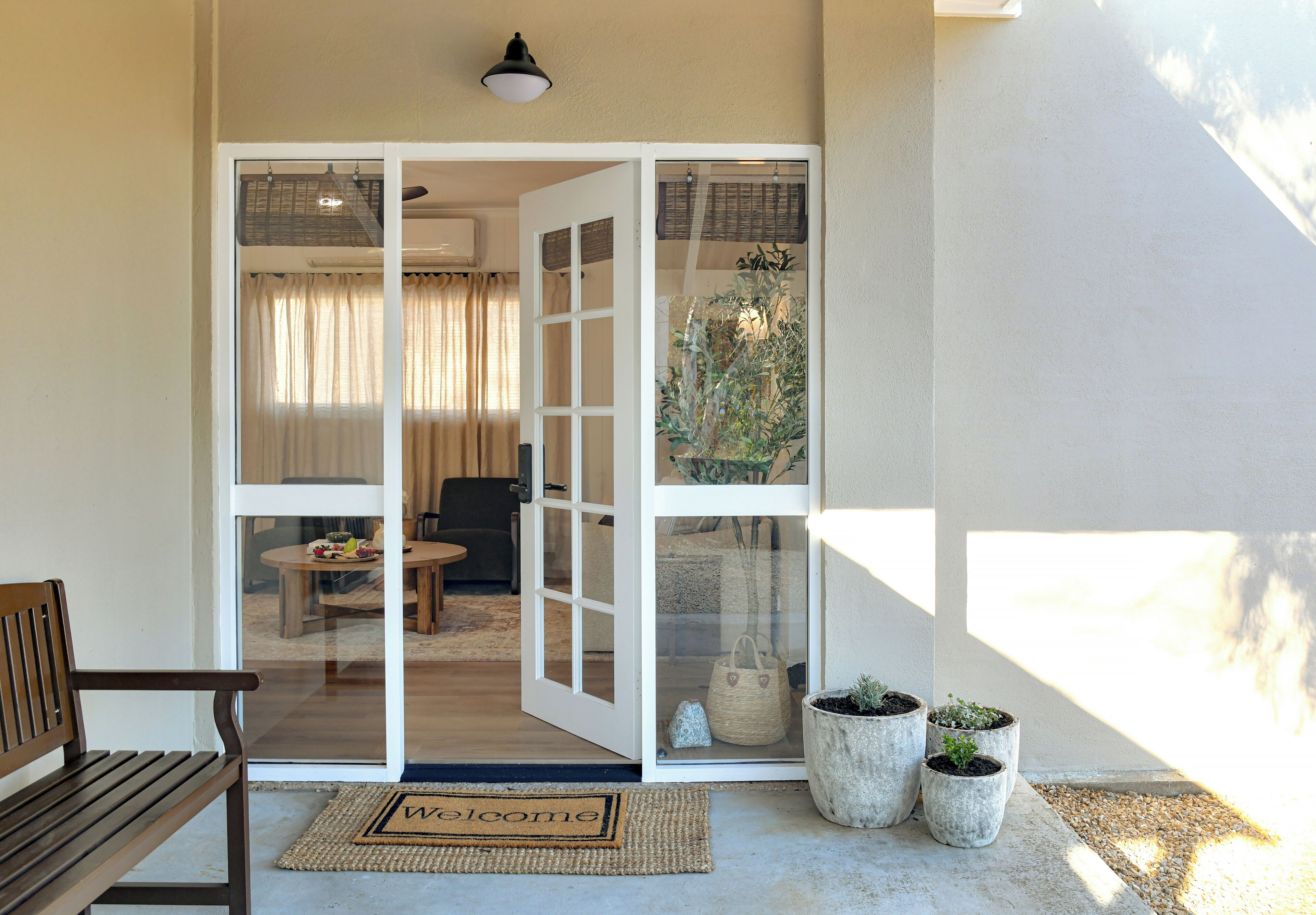 A doorway leading to a room with a dining table and chairs, a bench outside, and potted plants on the ground.