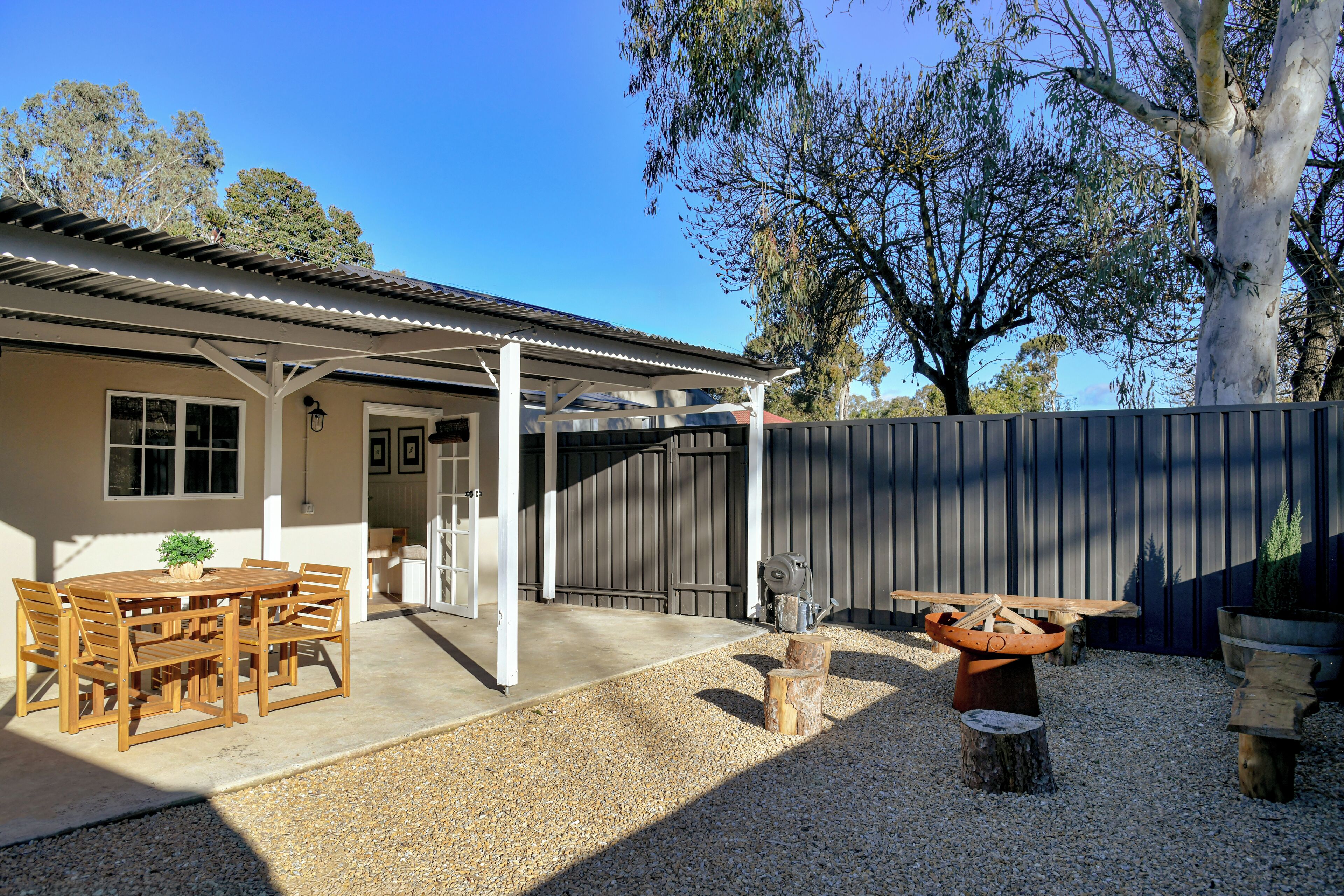 A covered outdoor patio with a table and chairs, a fire pit, and a gravel ground.