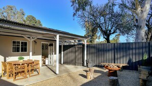 A covered outdoor patio with a table and chairs, a fire pit, and a gravel ground. - The Butcher's Cottage | New Barossa Valley Stay (Williamstown)