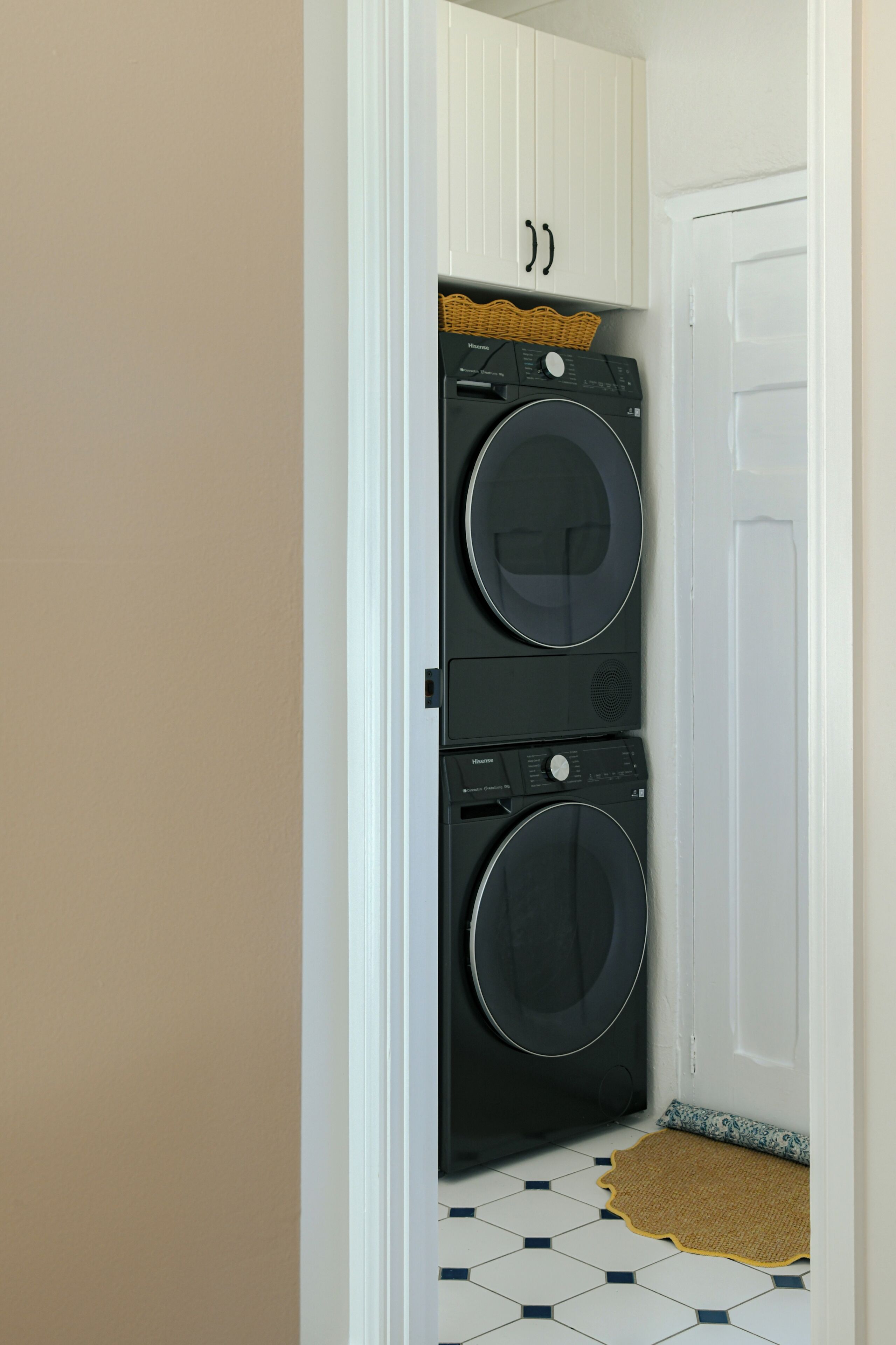 A compact laundry room with a double Hisense washing machine, a white door, and a tiled floor.