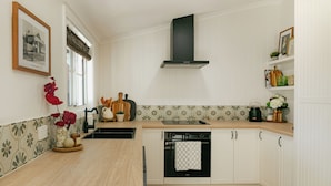 A kitchen with white cabinets, a black range hood, a wooden countertop, and a tiled backsplash. - The Butcher's Cottage | New Barossa Valley Stay (Williamstown)