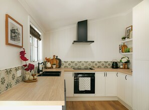 Una cocina con armarios blancos, una campana extractora negra, encimera de madera y salpicadero de azulejos.
